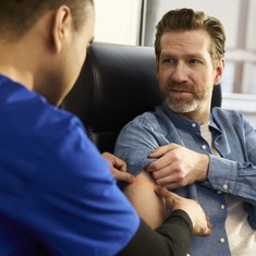 Une infirmière de la clinique INVIVA assise aux côtés d'un patient dans un fauteuil d'infusion, le patient souriant à l'infirmière. 