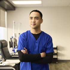 A male nurse standing in front of infusion chairs at one of our INVIVA clinics, smiling into the horizon with his arms crossed. 