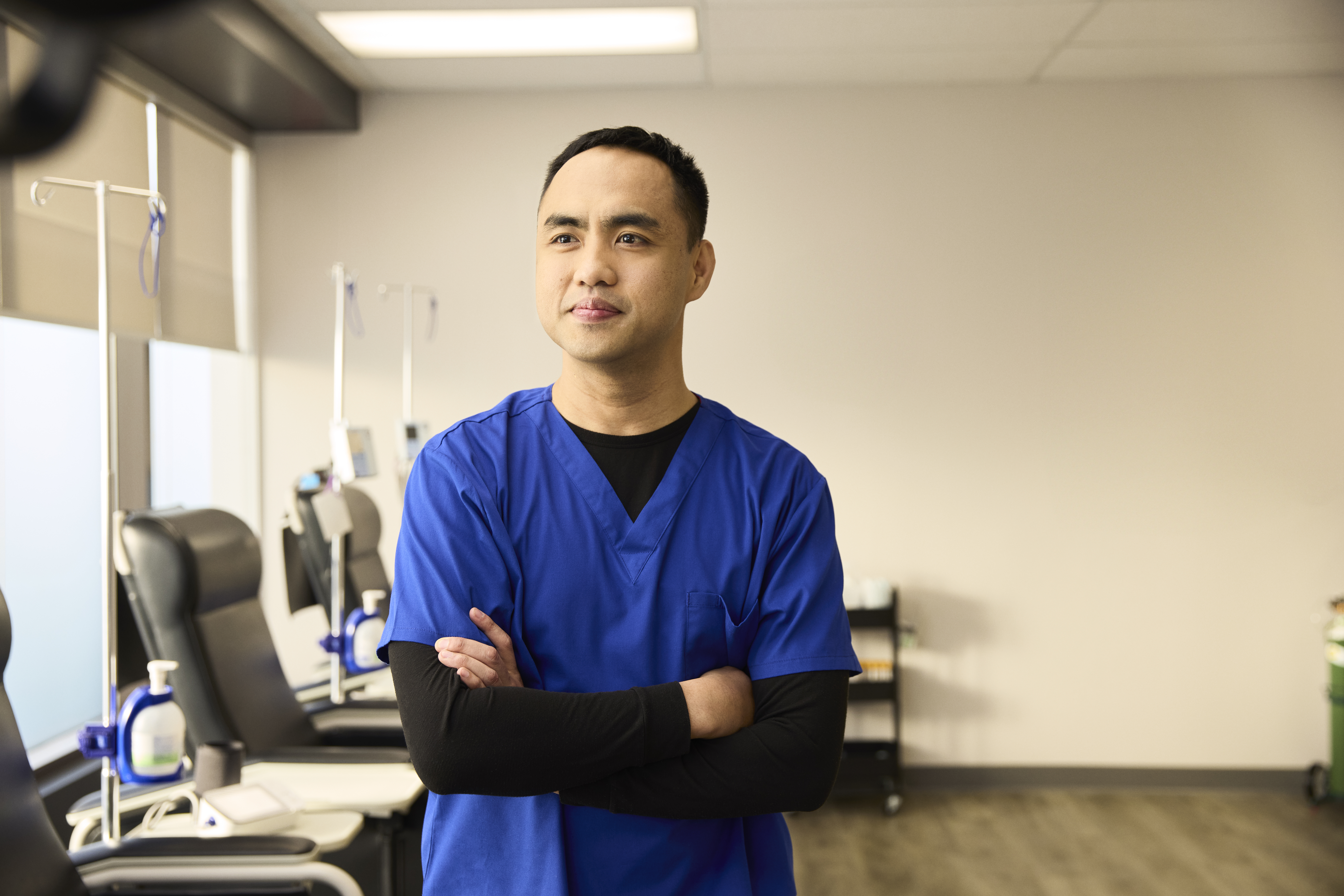 A male nurse standing in front of infusion chairs at one of our INVIVA clinics, smiling into the horizon with his arms crossed. 