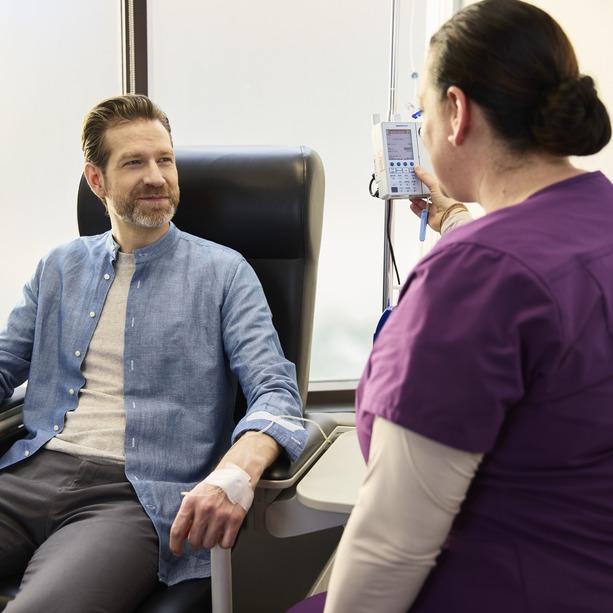 Une infirmière de la clinique INVIVA est assise à côté d'un patient dans un fauteuil d'infusion, avec le patient souriant à l'infirmière. 