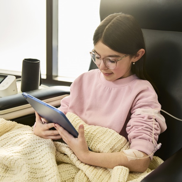 Young pediatric patient sitting on infusion chair receiving treatment while browsing on an iPad. 