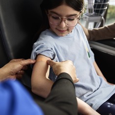 Pediatric patient looking at her arm while nurse places a Band-Aid to cover injection point. 